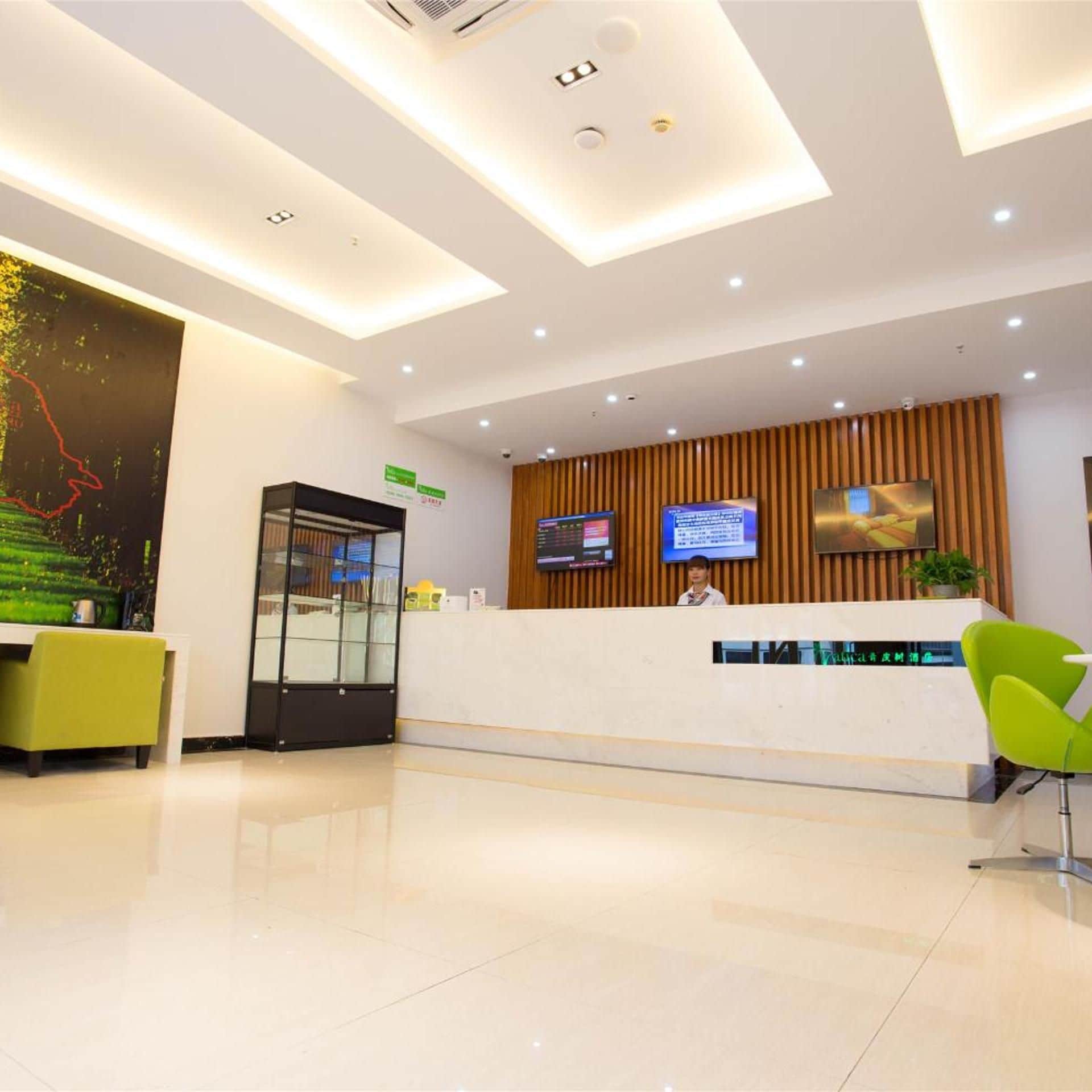 A modern reception area with a glass partition, a reception desk, two monitors, and a green chair.