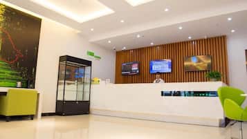 A modern reception area with a glass partition, a reception desk, two monitors, and a green chair.