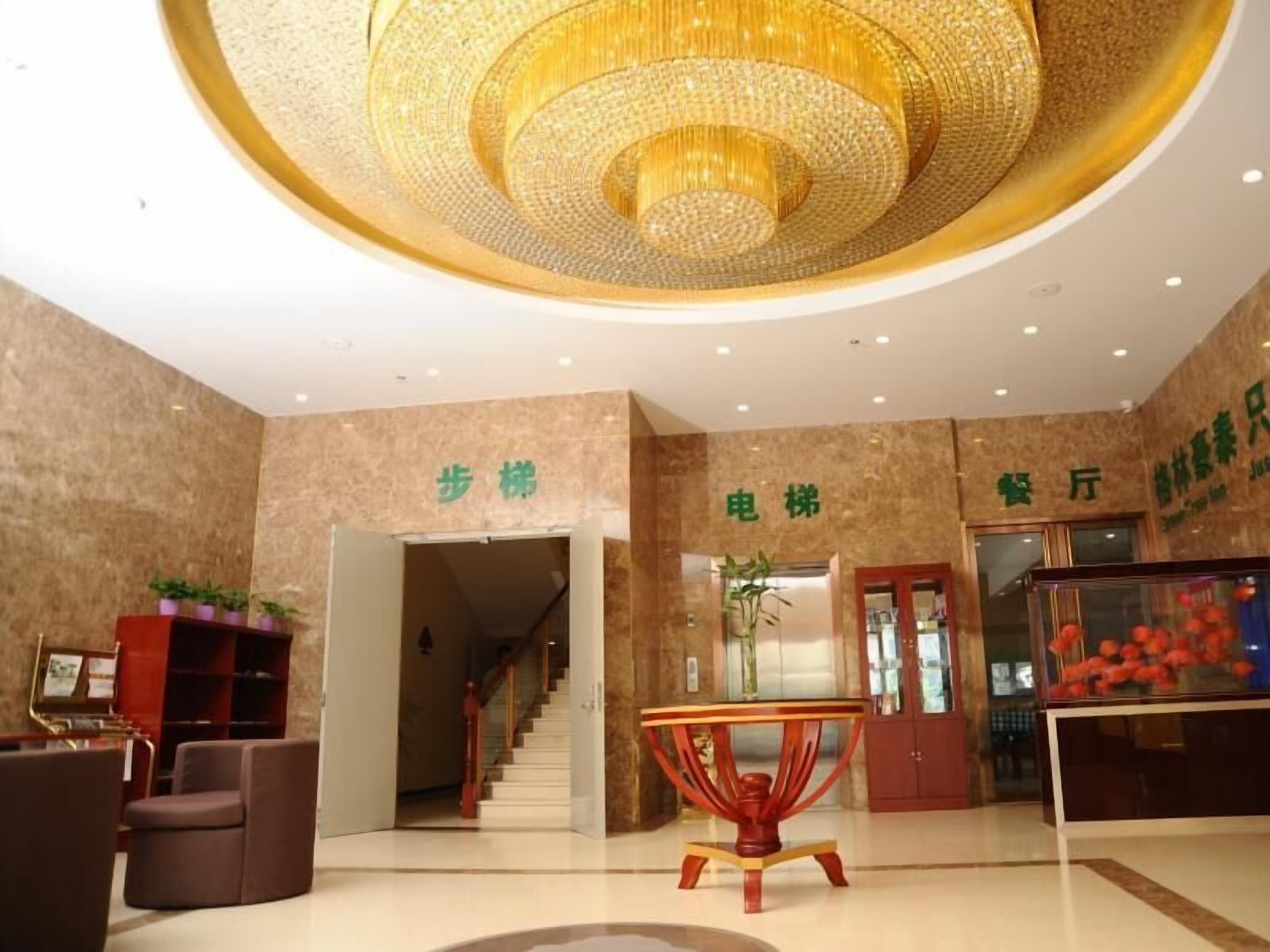 A hotel lobby with a chandelier, a reception desk, a staircase, and a dining area.