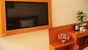A room with a mounted flat-screen TV, a wooden console table with a vase of flowers, a kettle, and a plant. - Greentree Inn Langfang Yanjiao Tianyang Plaza Expr (Langfang)