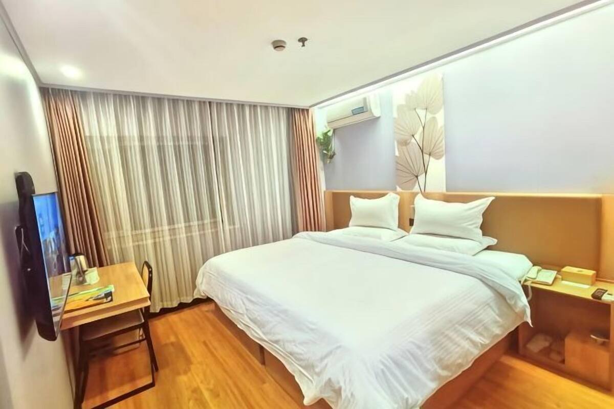Une chambre d’hôtel avec un lit, un bureau, une chaise, une télévision et une fenêtre avec des rideaux.