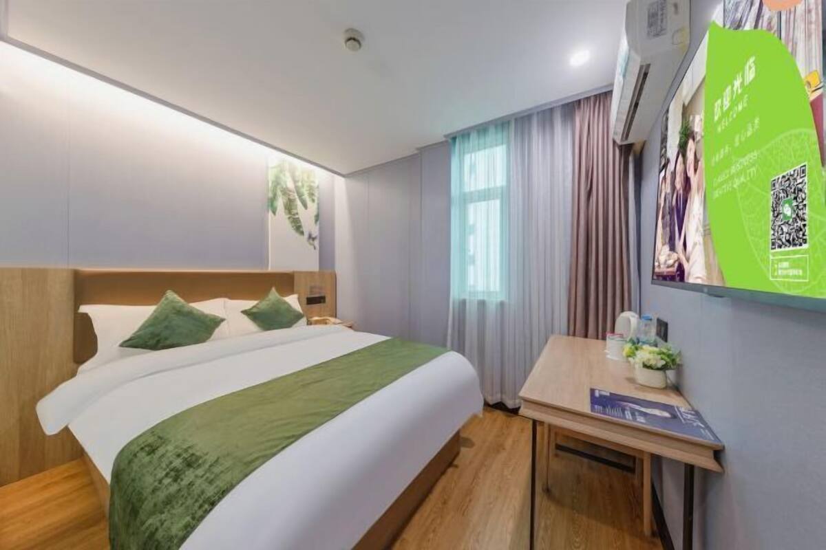 Une chambre d’hôtel équipée d’un lit, d’un bureau, d’un climatiseur fixé au mur et d’une fenêtre avec des rideaux.