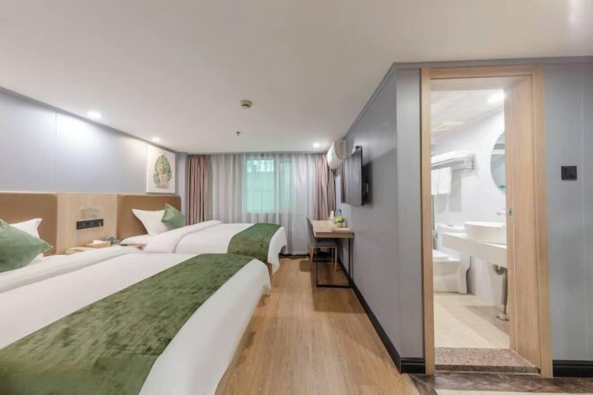 Une chambre d’hôtel avec deux lits, un bureau, un miroir et une salle de bain visible à travers une porte ouverte.