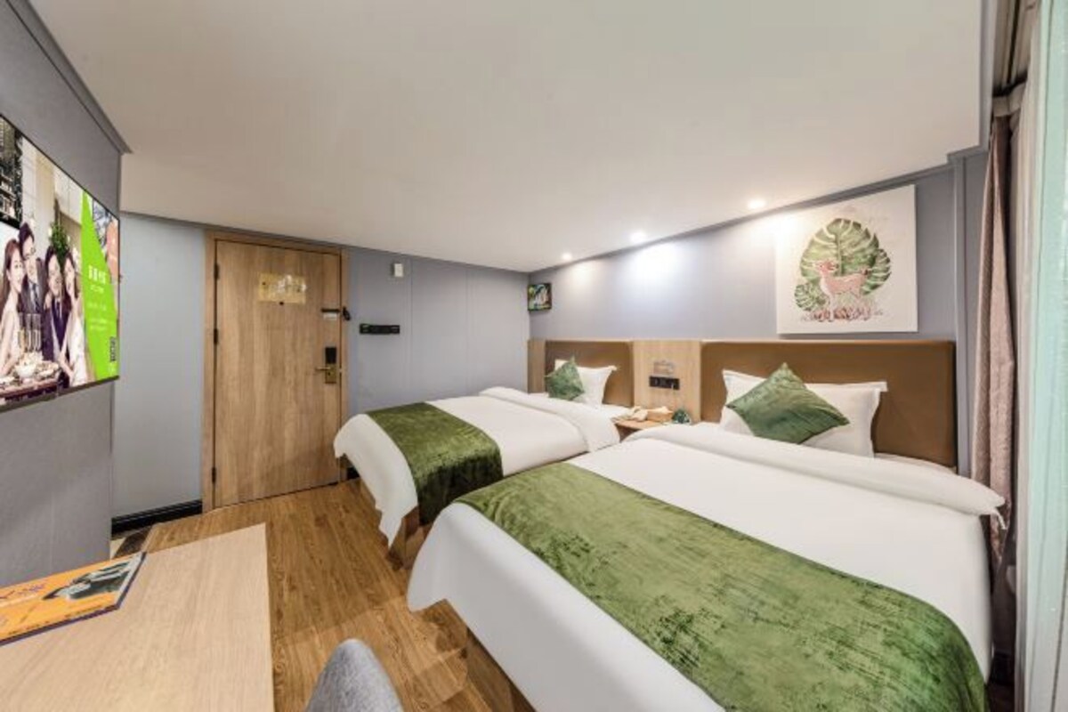 A hotel room with two beds, a wooden door, a small table, and a wall with a framed picture.