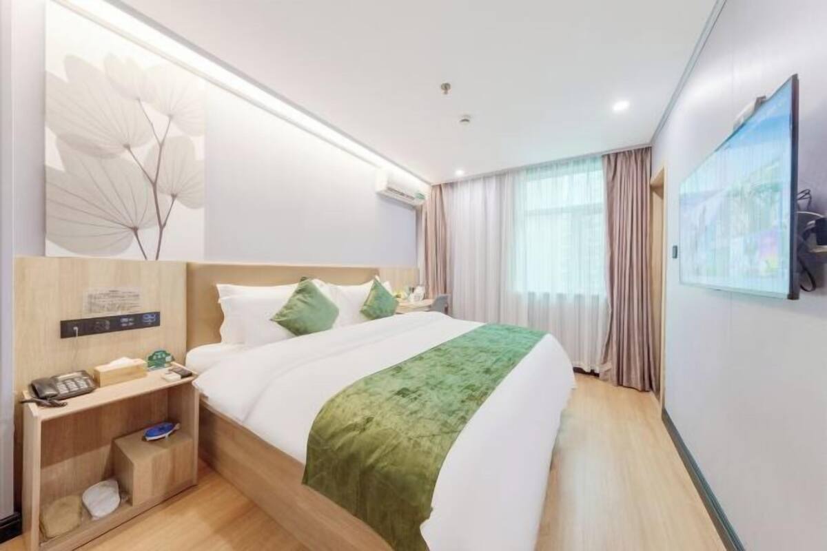 Une chambre d’hôtel avec un lit, une table de chevet, un téléviseur fixé au mur et une fenêtre avec des rideaux.