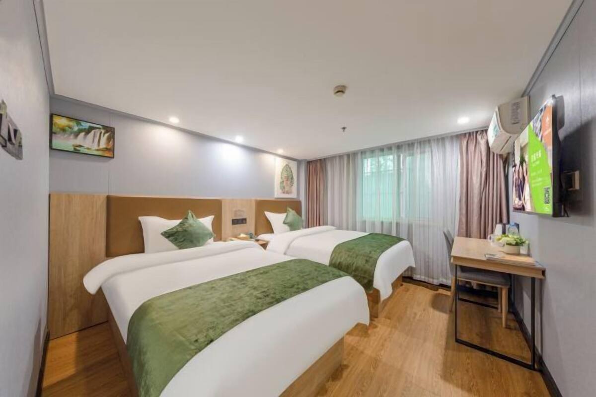 Une chambre d’hôtel avec deux lits, un bureau, une télévision et une fenêtre avec des rideaux.
