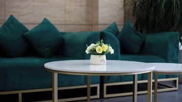 A green sofa with a white vase of flowers in front of it.