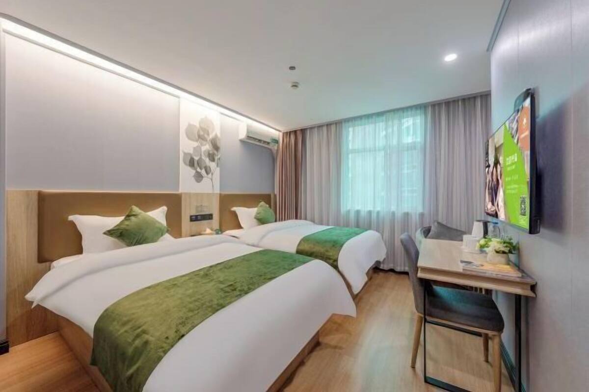 Une chambre d’hôtel avec deux lits, un bureau, une chaise, une télévision et une fenêtre avec des rideaux.