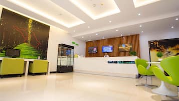 A modern reception area with a reception desk, green chairs, a large digital screen, and a mural on the wall.