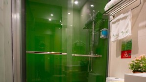 Un baño moderno con ducha de vidrio, inodoro blanco, cesta de mimbre con una toalla y una planta en maceta.