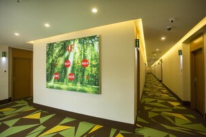Un pasillo de hotel con alfombra estampada, un cartel grande con círculos rojos y puertas a la derecha.