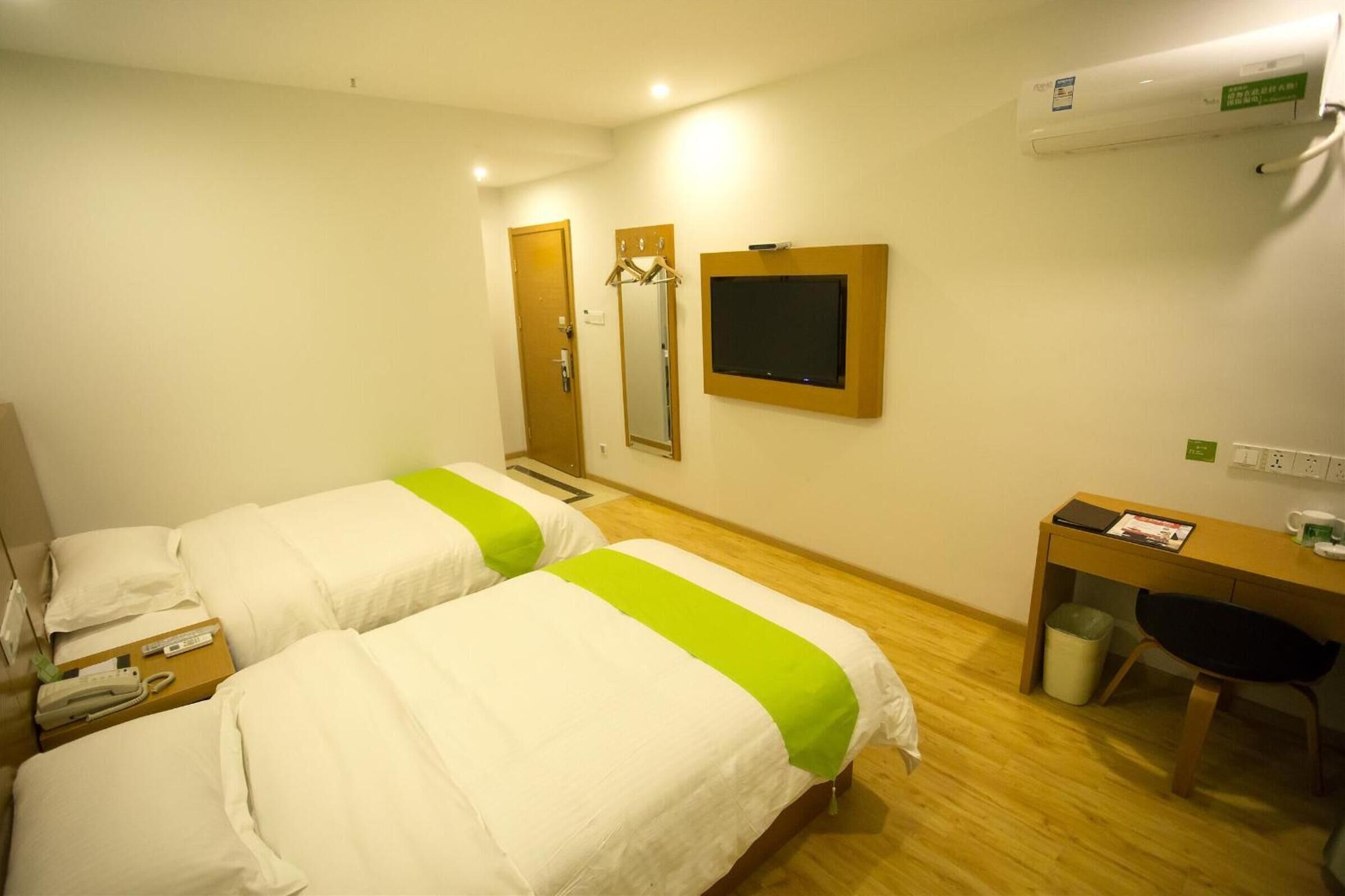 A hotel room with two beds, a desk, a chair, a mirror, and a television.
