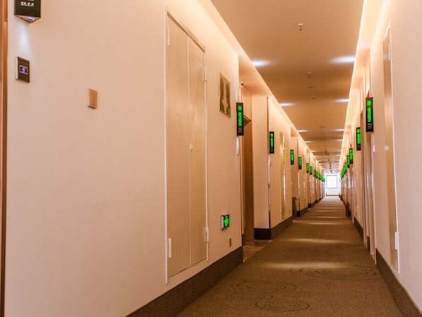 Een lange, goed verlichte hotelgang met deuren die verschillende kamers aangeven, een vloerbedekking en een plafond met inbouwspots.