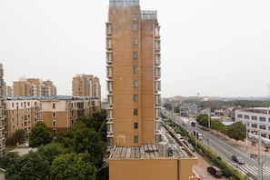 Un edificio residencial alto con varios balcones, rodeado de otros edificios similares y una calle con coches y árboles.