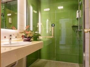 A bathroom with a green tiled wall, a sink with a mirror, a potted plant, and a shower area. - Greentree Inn Changzhou Wujin District Huangli Town Taoyuan Road Express Hotel (Changzhou)