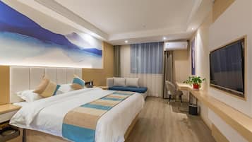 A hotel room with a large bed, a smaller bed, a desk with a chair, an air conditioning unit, a TV, and a painting on the wall.