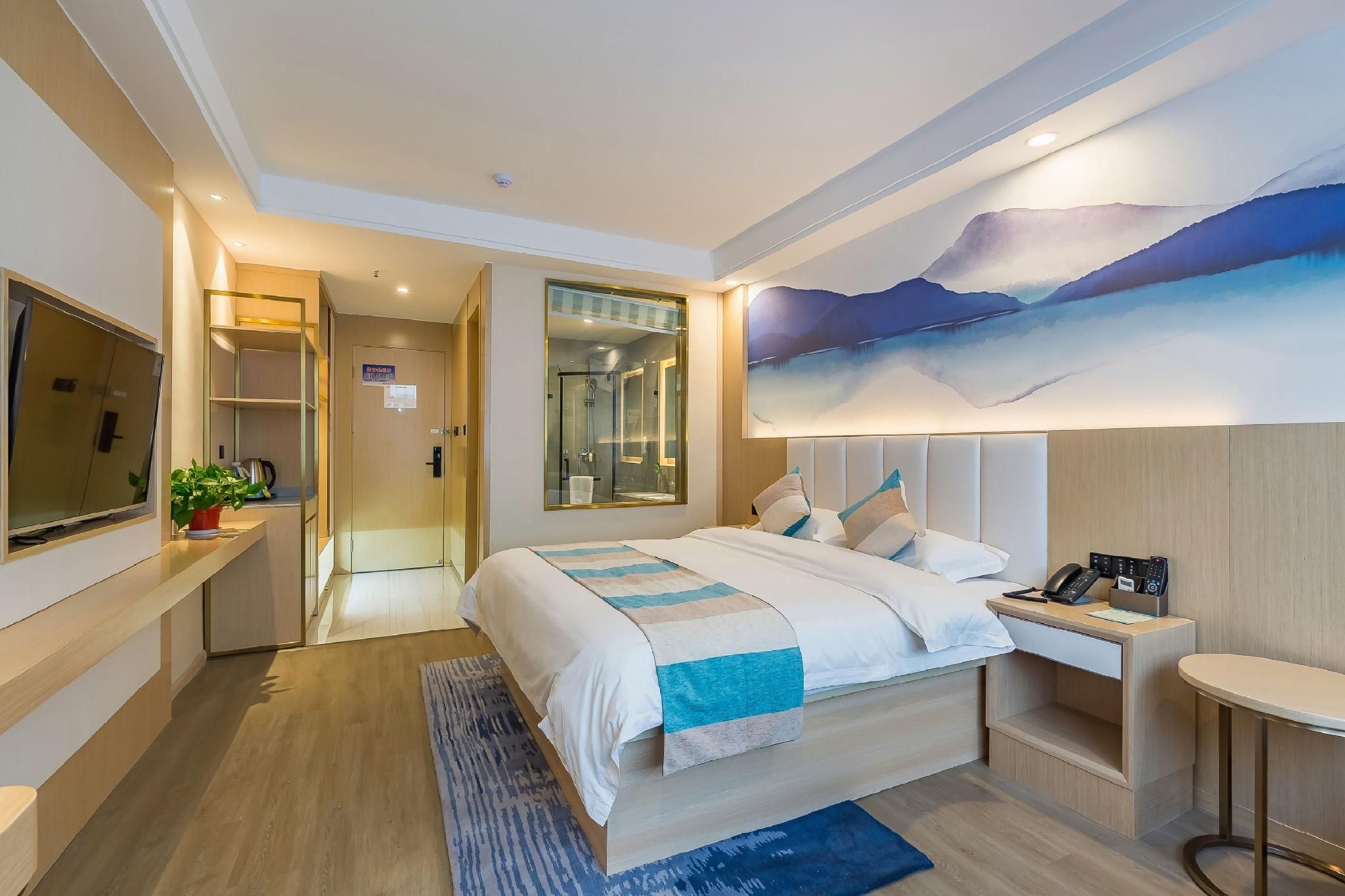 A modern hotel room with a large bed, a desk, a flat-screen TV, and a painting on the wall.