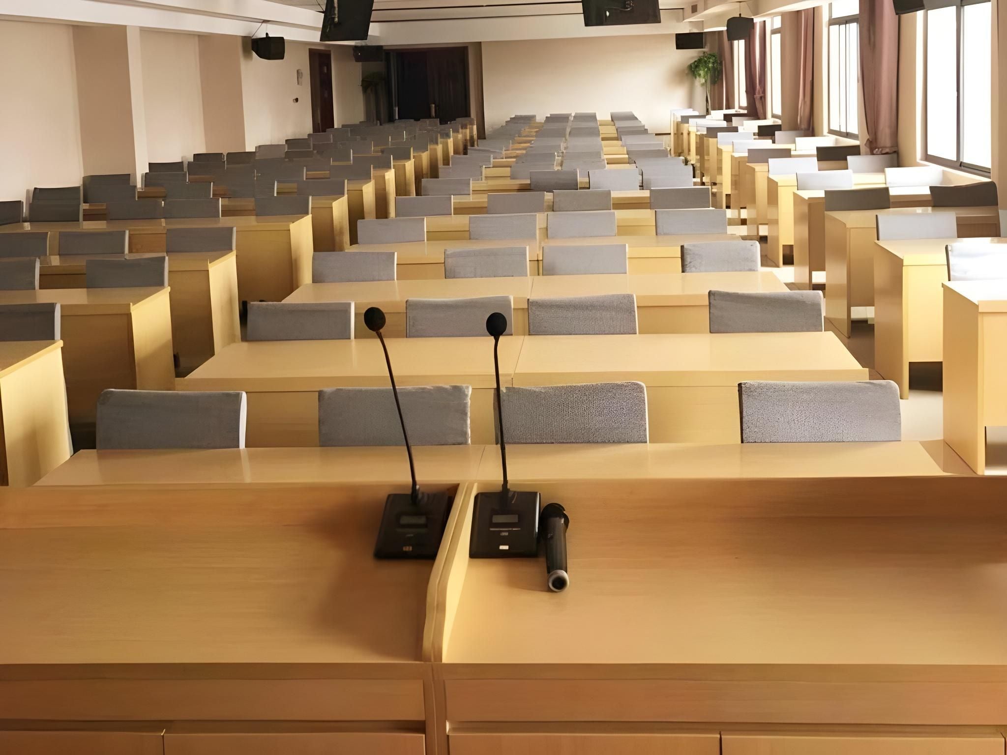 A lecture hall with rows of desks and chairs, equipped with microphones and a projector.