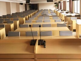 Un auditorio con filas de escritorios y sillas, equipado con micrófonos y un proyector.
