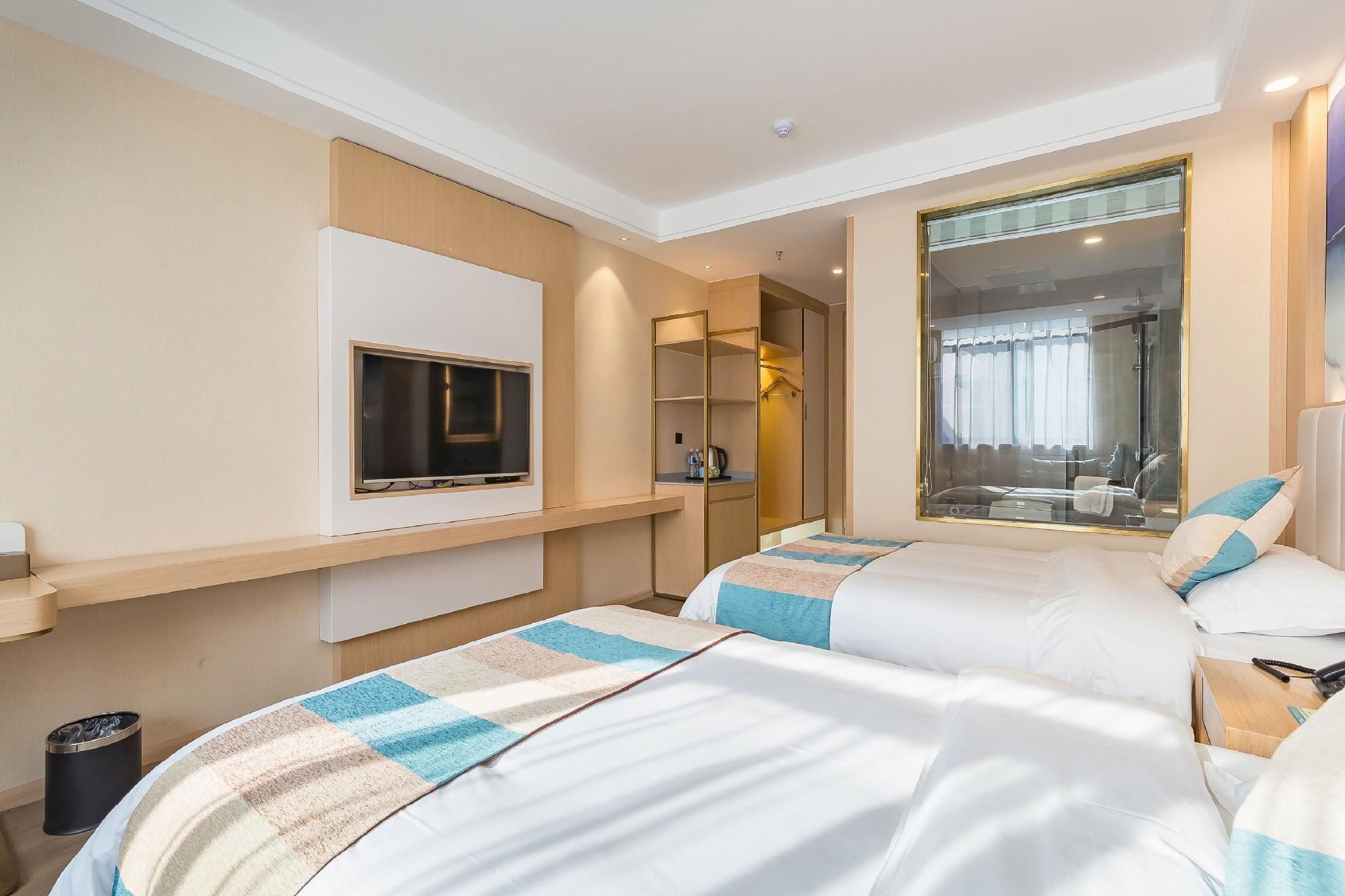 Une chambre d’hôtel avec deux lits, une télévision, un miroir et une fenêtre donnant sur une salle de bain.
