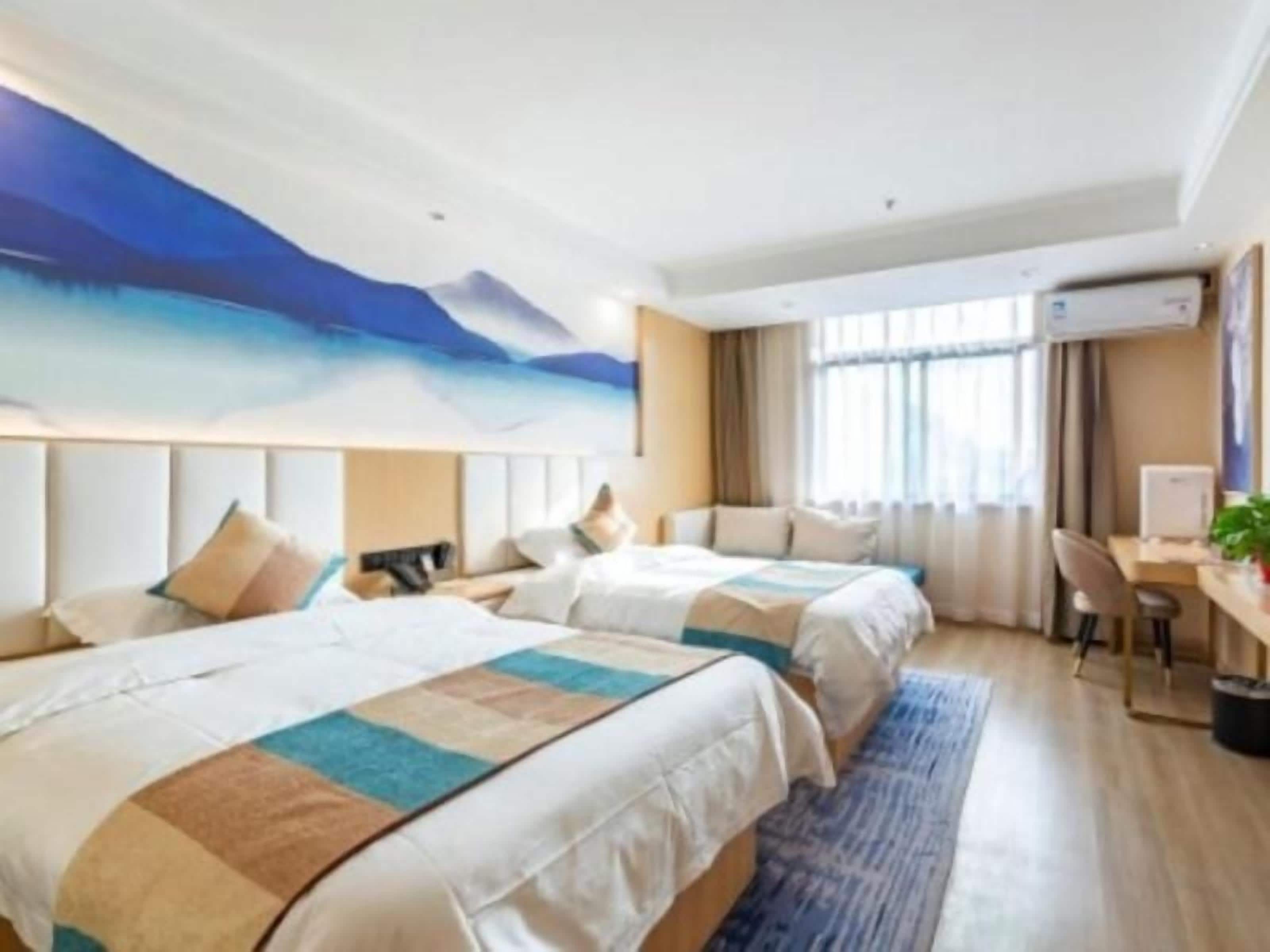 A hotel room with two beds, a desk, and a large window.