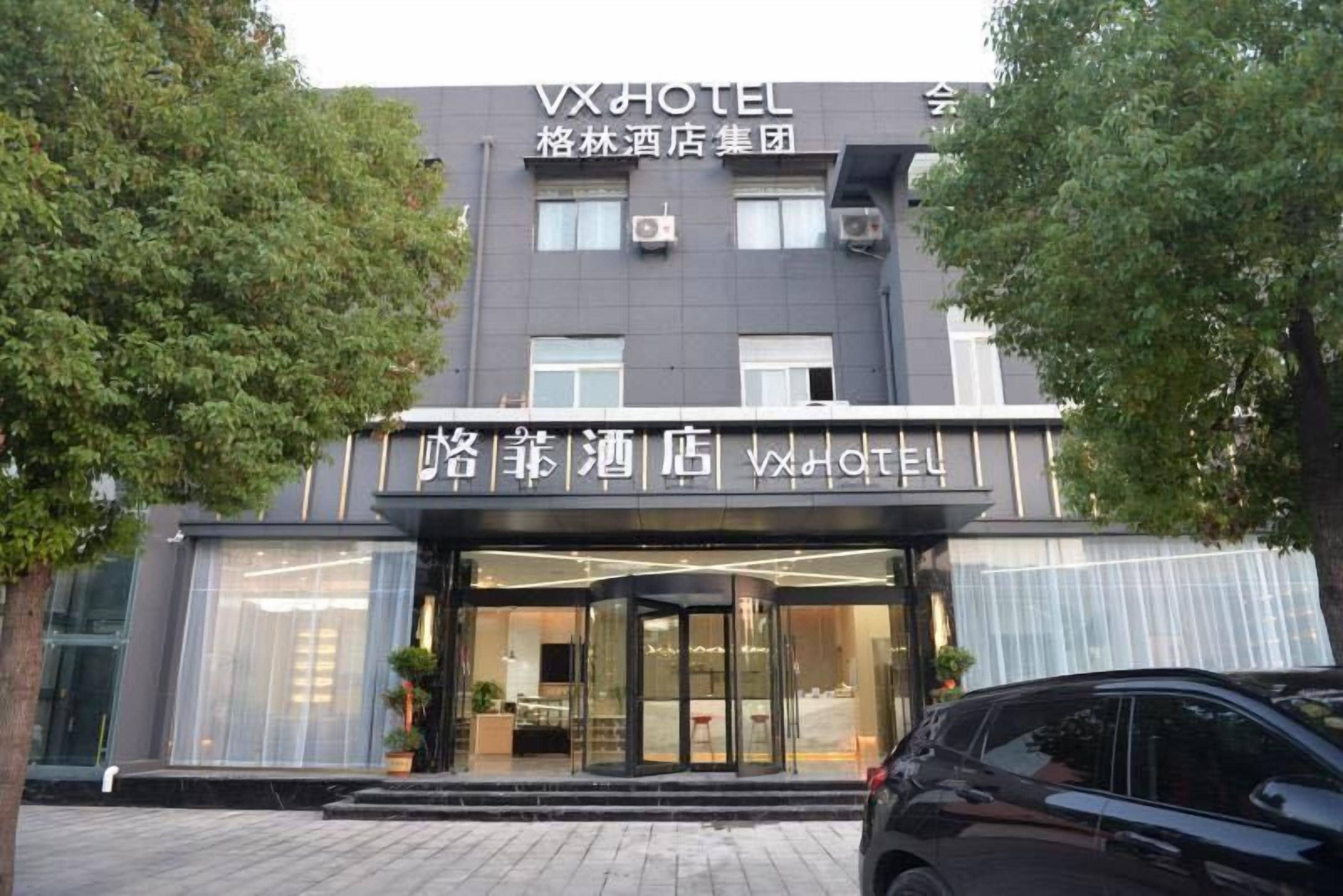 A hotel entrance with a modern facade, large glass windows, and a car parked in front.