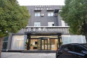 Entrada de hotel con fachada moderna, amplios ventanales y un coche estacionado al frente.