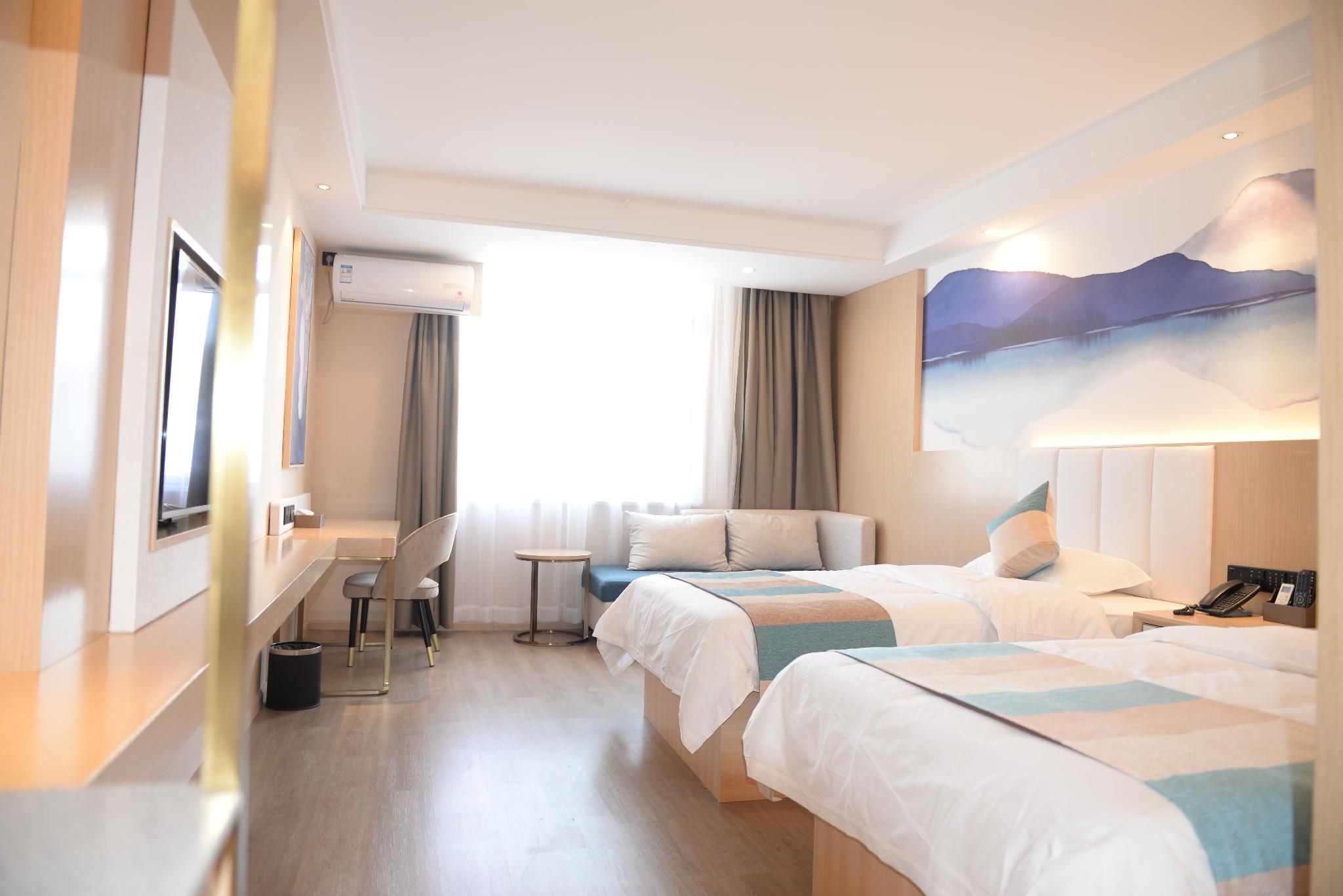 A hotel room with two beds, a desk, a chair, and a painting on the wall.