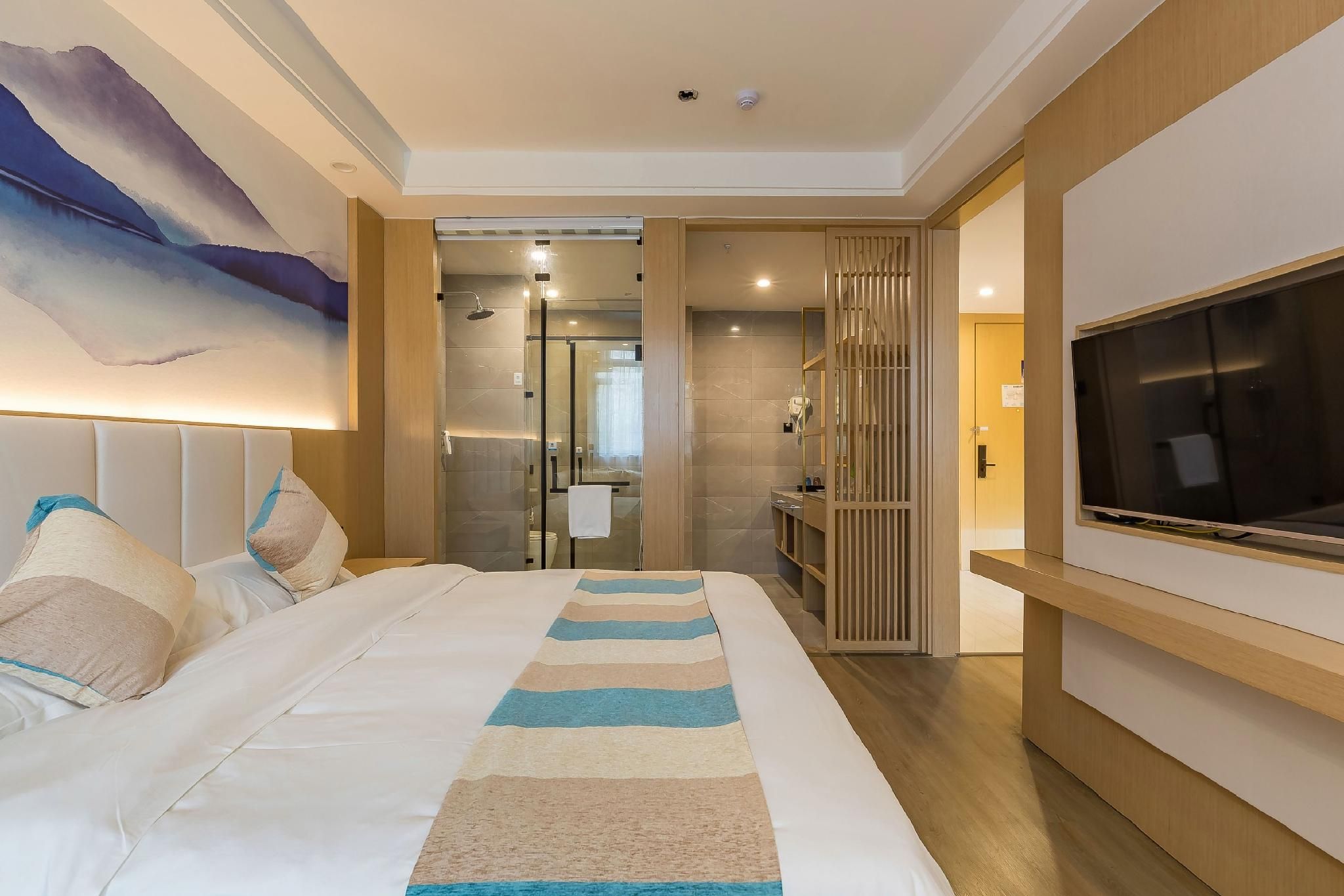 A hotel room with a large bed, a TV, a bathroom with a glass shower, and a painting on the wall.