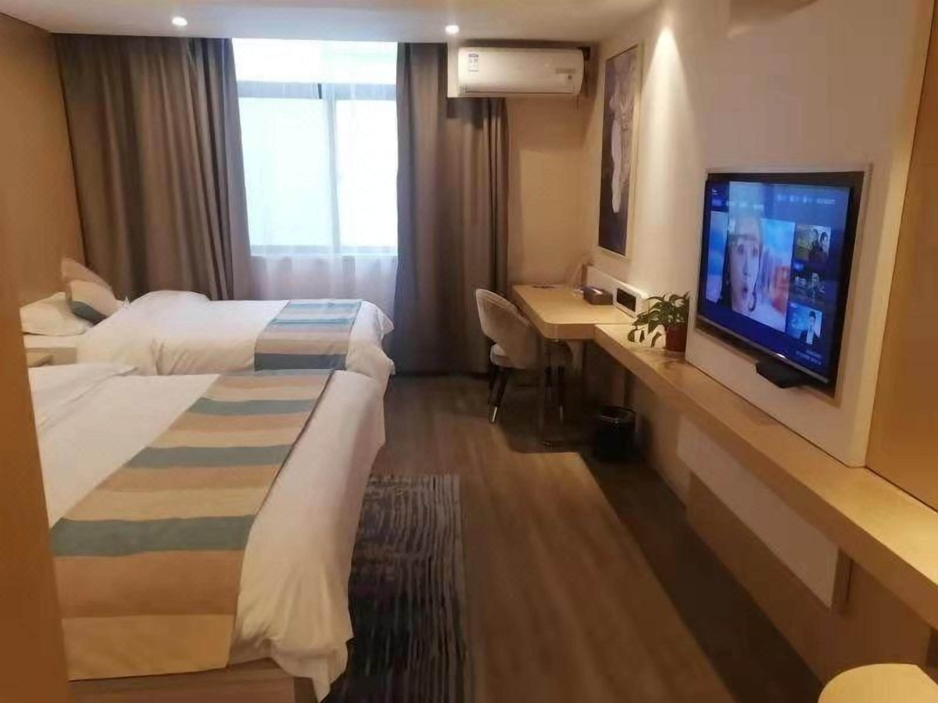 Habitación de hotel con dos camas, un escritorio, televisor y ventana con cortinas.
