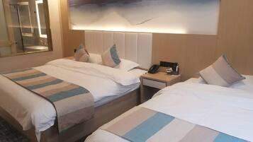 Habitación de hotel con dos camas, una mesita de noche con un teléfono y una lámpara, y un cuadro de paisaje grande en la pared.