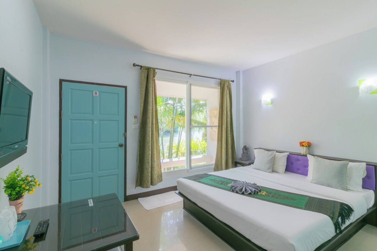 A hotel room with a bed, a television, a window with curtains, and a door.