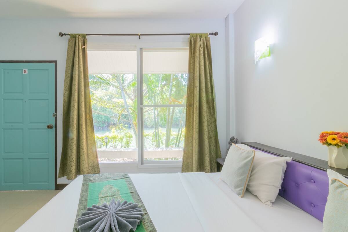 Une chambre d’hôtel avec un lit, une fenêtre avec des rideaux, une porte et un luminaire fixé au mur.