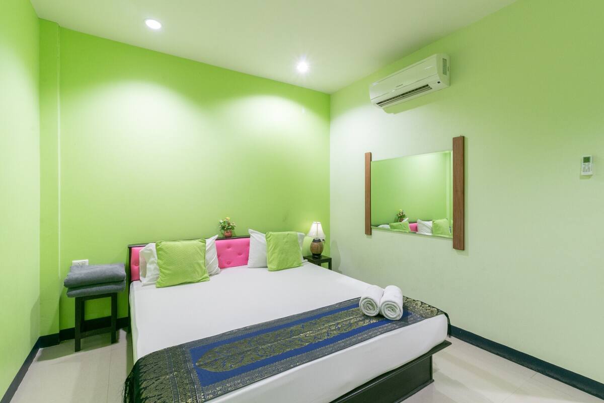 Une chambre d’hôtel comprenant un lit, une petite table avec une serviette, une table de chevet avec une lampe et un climatiseur fixé au mur.