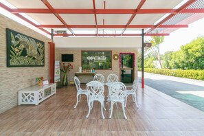 An outdoor seating area with white chairs and a table, a reception desk, and a wall-mounted TV. - Chaiyo Resort Phuket by Zuzu (Wichit)