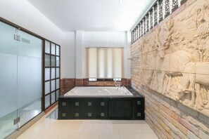 Un baño moderno con una bañera grande, mampara de cristal para la ducha y una pared decorativa de piedra.