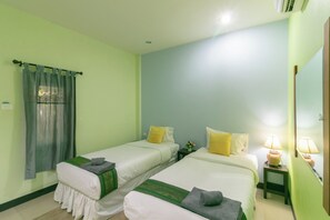 Ein Hotelzimmer mit zwei Betten, einem kleinen Tisch, einem Nachttisch, einem Spiegel und einem Fenster mit Vorhängen.