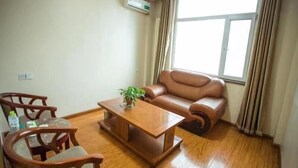 A living room with a wooden coffee table, two wooden chairs, a leather sofa, a potted plant, and a large window with curtains.