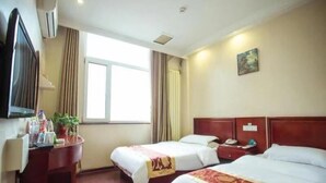A hotel room with two beds, a desk with a TV, and a window with curtains.