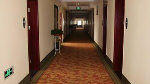 Ein Hotelkorridor mit Teppichböden, rechts und links Türen und einer Pflanze in der Mitte.