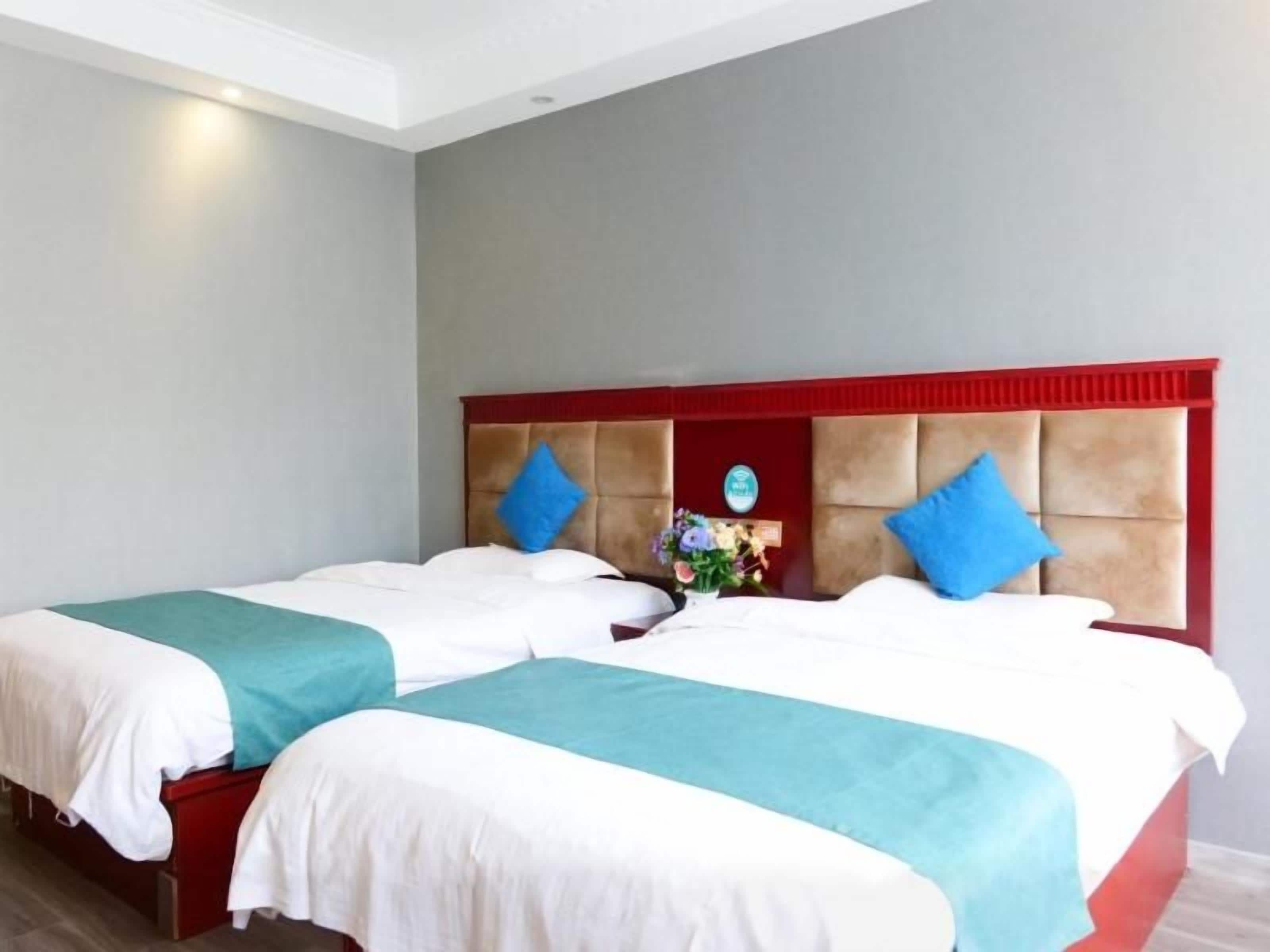 A double bed with a red headboard, two pillows, and a nightstand with a vase of flowers.