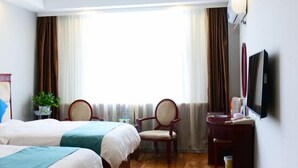 Ein Hotelzimmer mit zwei Betten, einem Schreibtisch, einem Sessel, einem Fernseher und einem Fenster mit Vorhängen.