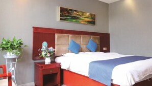 Habitación de hotel con cama, mesita de noche con un florero, una silla roja y un cuadro en la pared.