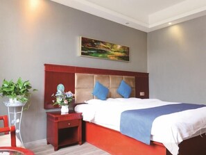 Une chambre d’hôtel avec un lit, une table de chevet ornée d’un vase de fleurs, un fauteuil rouge et un tableau accroché au mur.