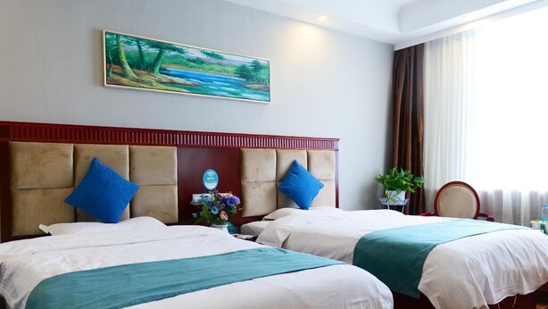 Habitación de hotel con dos camas, un cuadro en la pared, una planta y vistas al exterior.