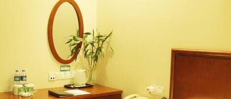 A hotel room with a bed, a desk with a mirror, a telephone, a remote control, and a plant.