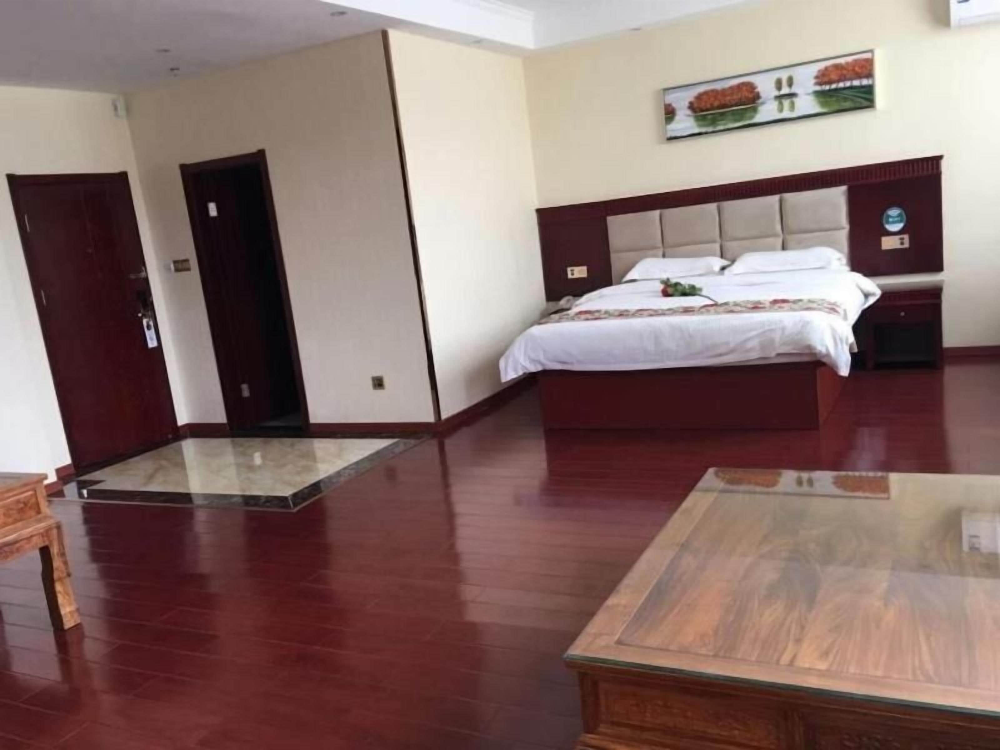 A hotel room with a large bed, a wooden nightstand, a desk, and a door.