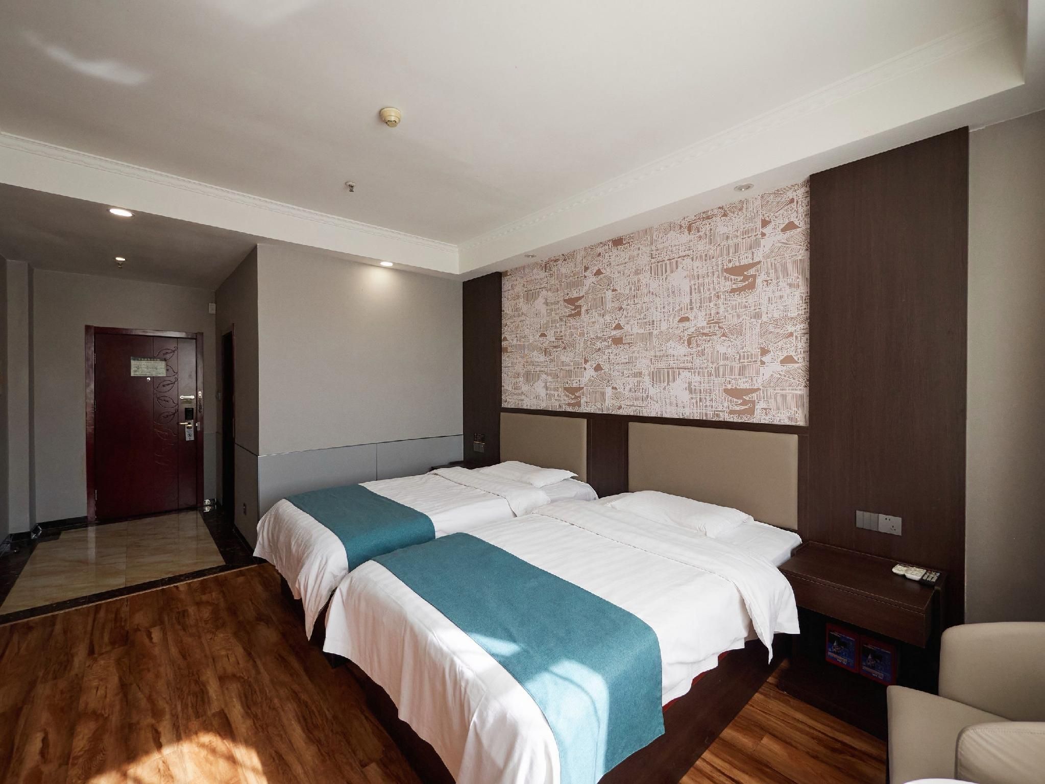 Habitación de hotel con dos camas, un mural grande en la pared, suelo de madera y una puerta.