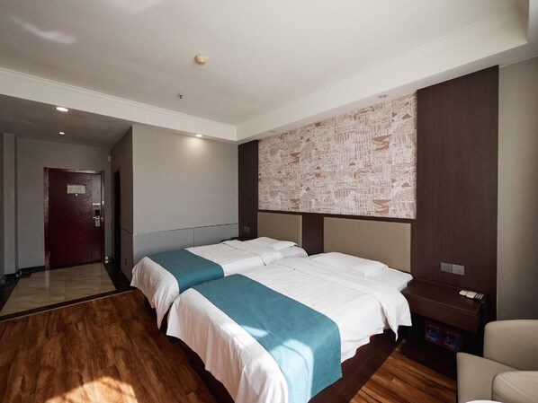 A hotel room with two beds, a large wall mural, a wooden floor, and a door.