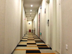 Et hotelkorydor med et ternet gulv, døre på begge sider og en rød nødudgangsskilte.